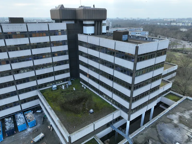 Aerial view of the high-rise before the retrofit: two wings with light concrete facing panels, a flat roof in front