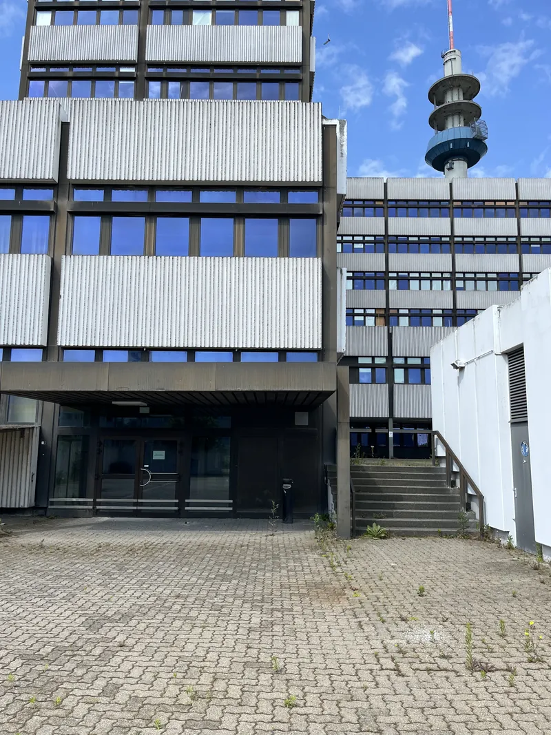 The building's entrance before the retrofit: canopy, steps and weeds in the paving