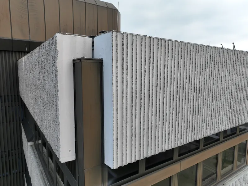 Building corner up close: two ribbed concrete facing panels with a pilaster strip between them